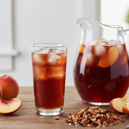 Iced tea with peaches in a glass and pitcher on a wooden surface.