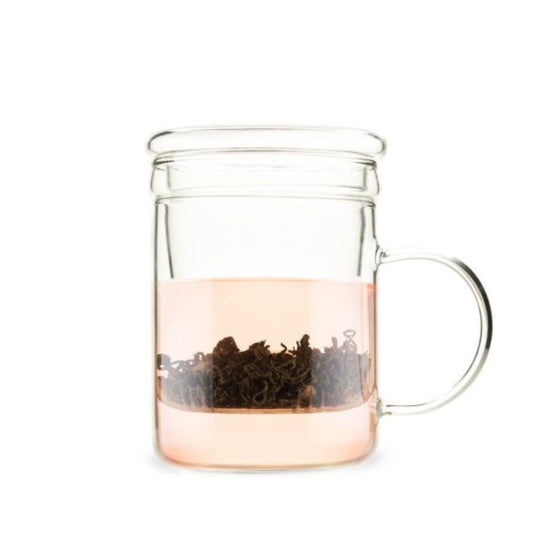 Clear glass mug with a handle containing black tea leaves on a white background