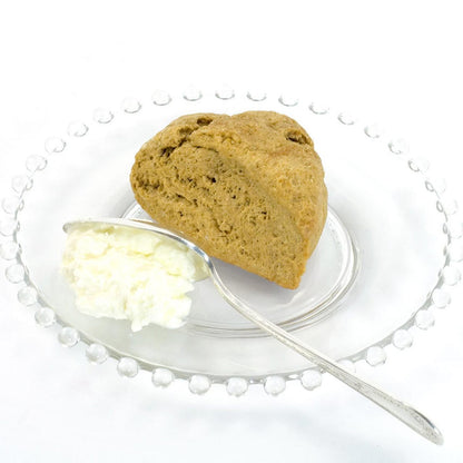 Baked scone with a side of cream on a white plate with a silver fork.