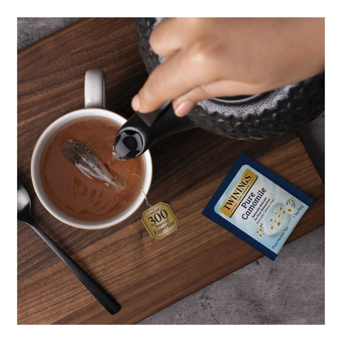 Tea being poured into a cup with Twinings tea packaging on a wooden surface