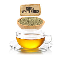Glass cup of tea with a wooden bowl of tea leaves and a bag labeled 'Kenya White Rhino' on a white background.