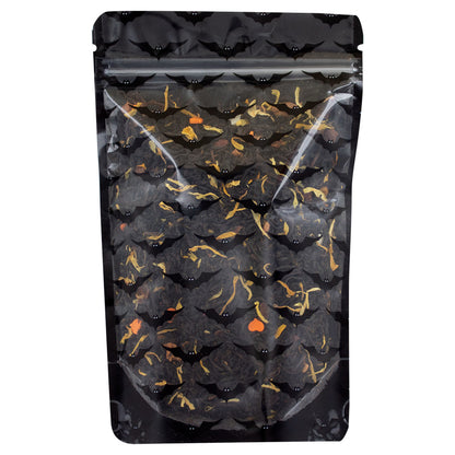 A mix of dried black tea leaves and pieces of fruit and herbs, including apple, orange, and hibiscus, indicative of a spicy flavored tea in a sealed pouch with transparent front and black bat designs and a black backing on a white background.