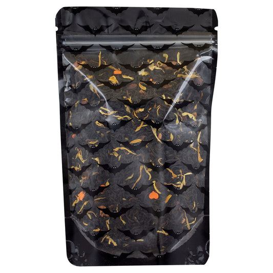 A mix of dried black tea leaves and pieces of fruit and herbs, including apple, orange, and hibiscus, indicative of a spicy flavored tea in a sealed pouch with transparent front and black bat designs and a black backing on a white background.
