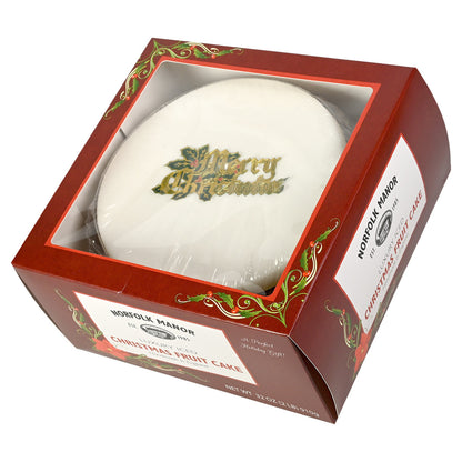 A red box of Norfolk Manor Christmas Fruit Cake with a translucent plastic window displaying the white icing of the cake with a decorative Merry Christmas topper.