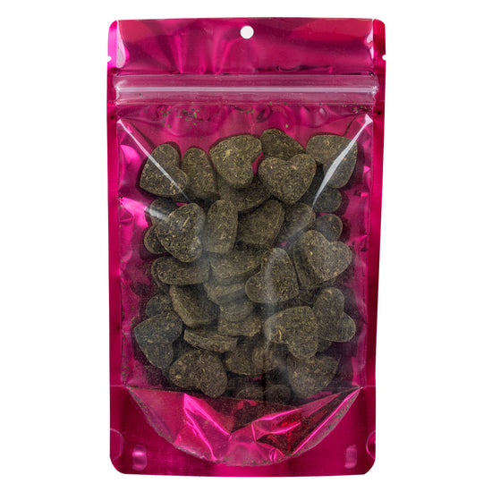 Pink transparent bag with heart-shaped dark green tea leaves pressed into hearts with the package on a white background