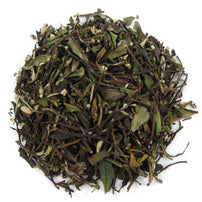 A pile of dry loose leaf tea with visible pieces of green tea leaves and small white tea buds.