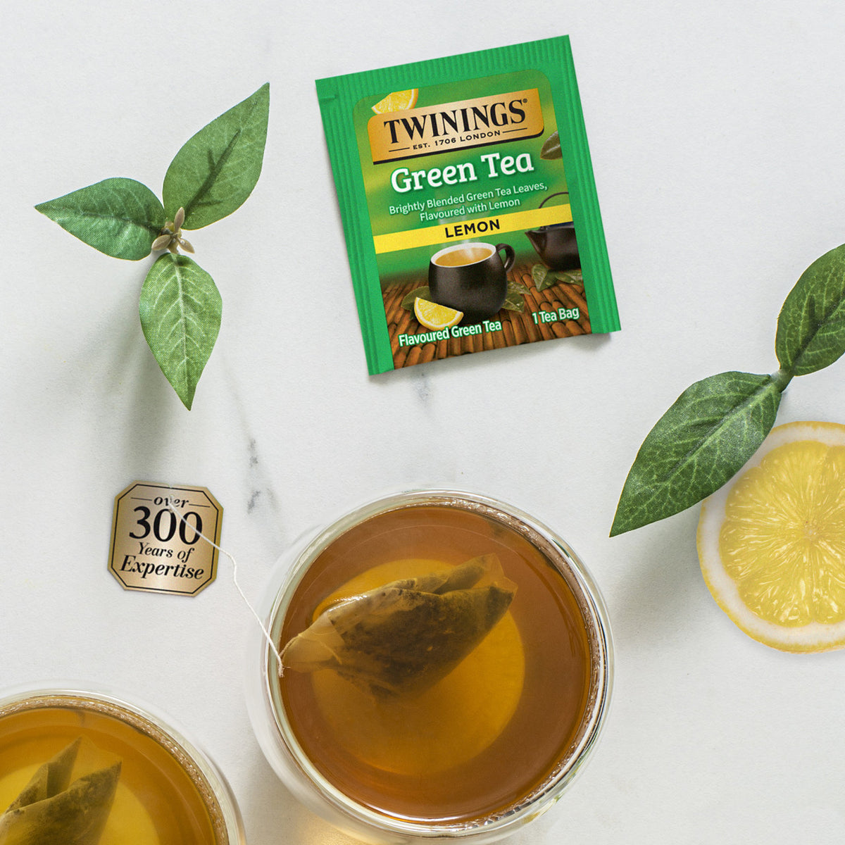 Twinings Green Tea Lemon packet with a cup of tea and lemon slices on a white background