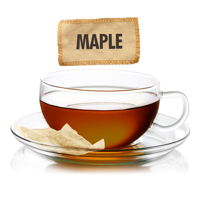 Glass cup of Sugar Shack Smokey Maple Black Tea amber colored with a 'Maple' labeled tea bag on a white background