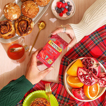 Person holding Twinings Christmas Tea box with festive food and drinks on a table