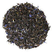 Dry black tea leaves with purple peddles in a circular pattern on a white backround.