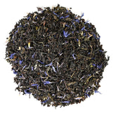 Dry black tea leaves with purple peddles in a circular pattern on a white backround.