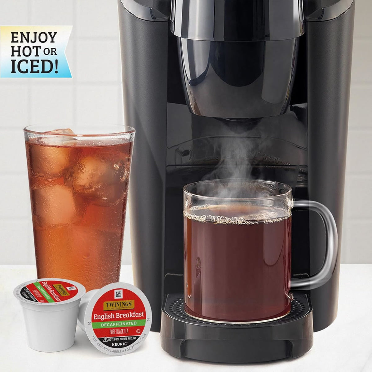 Black Keurig machine with a mug of hot black tea and a glass of iced tea, featuring Twinings tea packages.