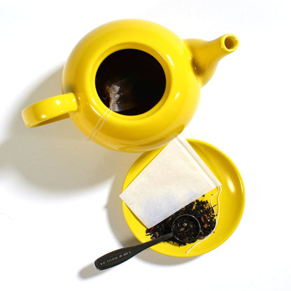 A pack of white drawstring tea filters displayed alongside a clear teapot with tea bags inside, indicating usage.