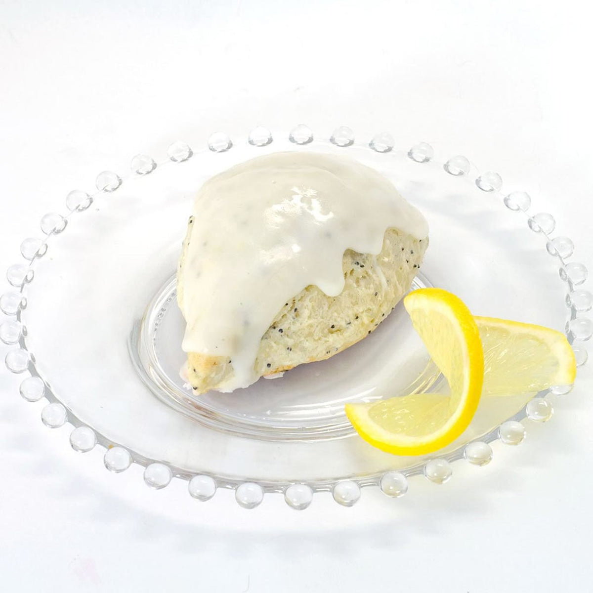 Baked lemon poppyseed scone with lemon glaze on a clear plate with a lemon wedge on a white background