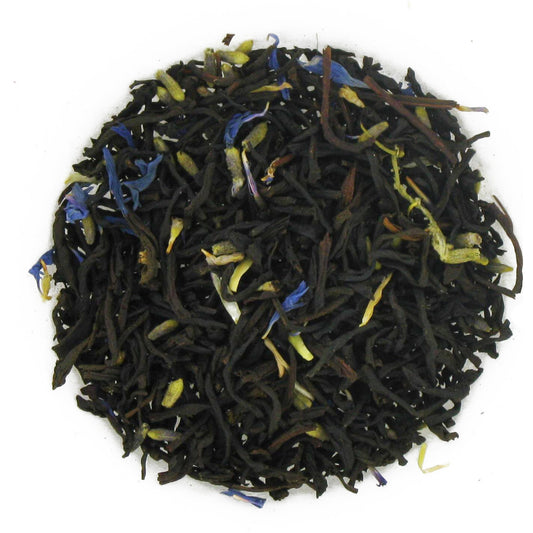 A mixture of dark black tea leaves and blue cornflower petals, arranged in a circular pattern.