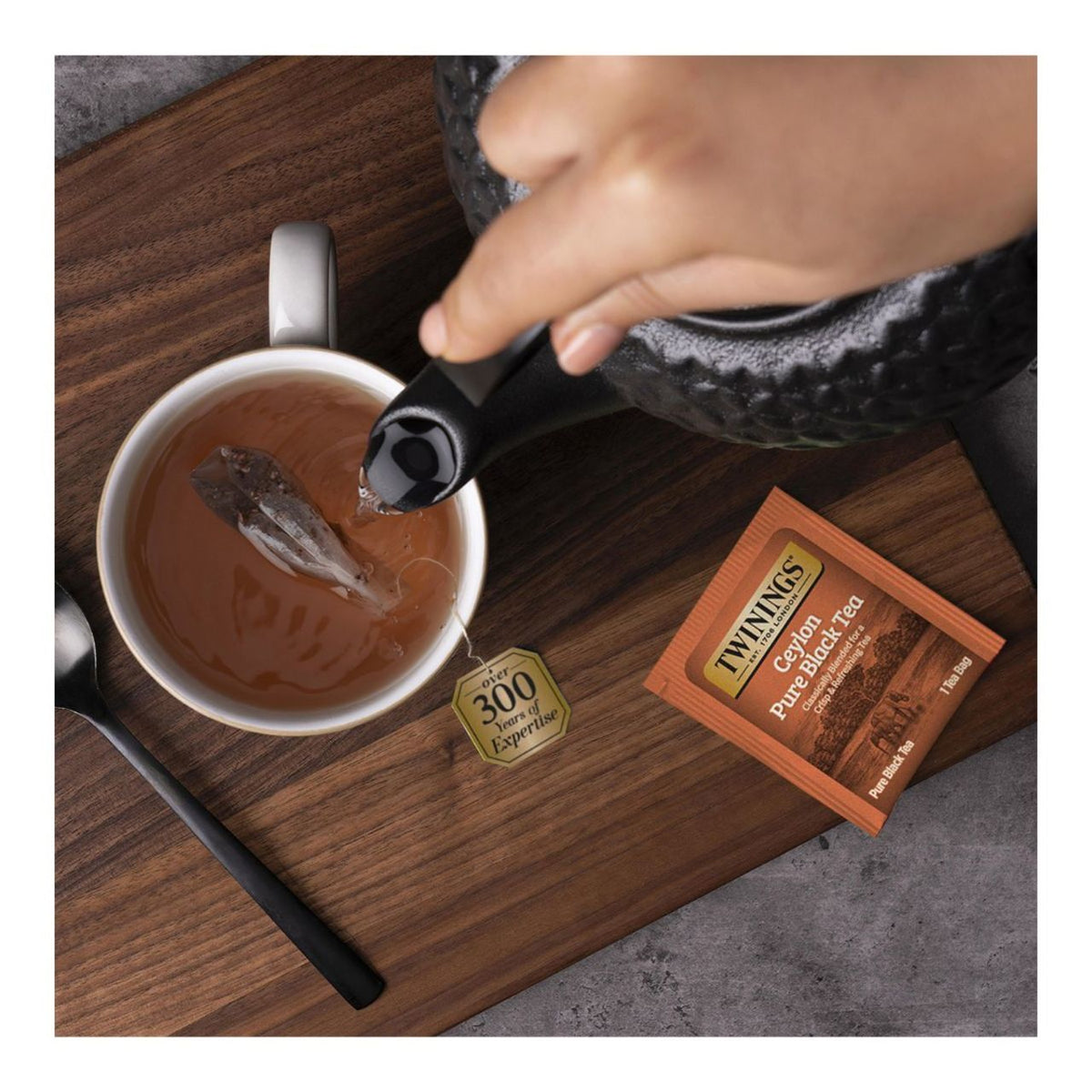 Tea being poured into a cup with Twinings tea packaging on a wooden surface