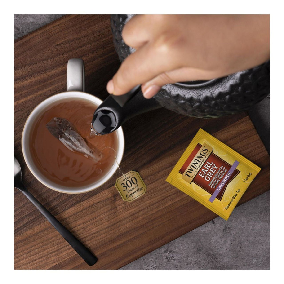Person pouring tea into a cup with Twinings Earl Grey tea bag on a wooden surface.
